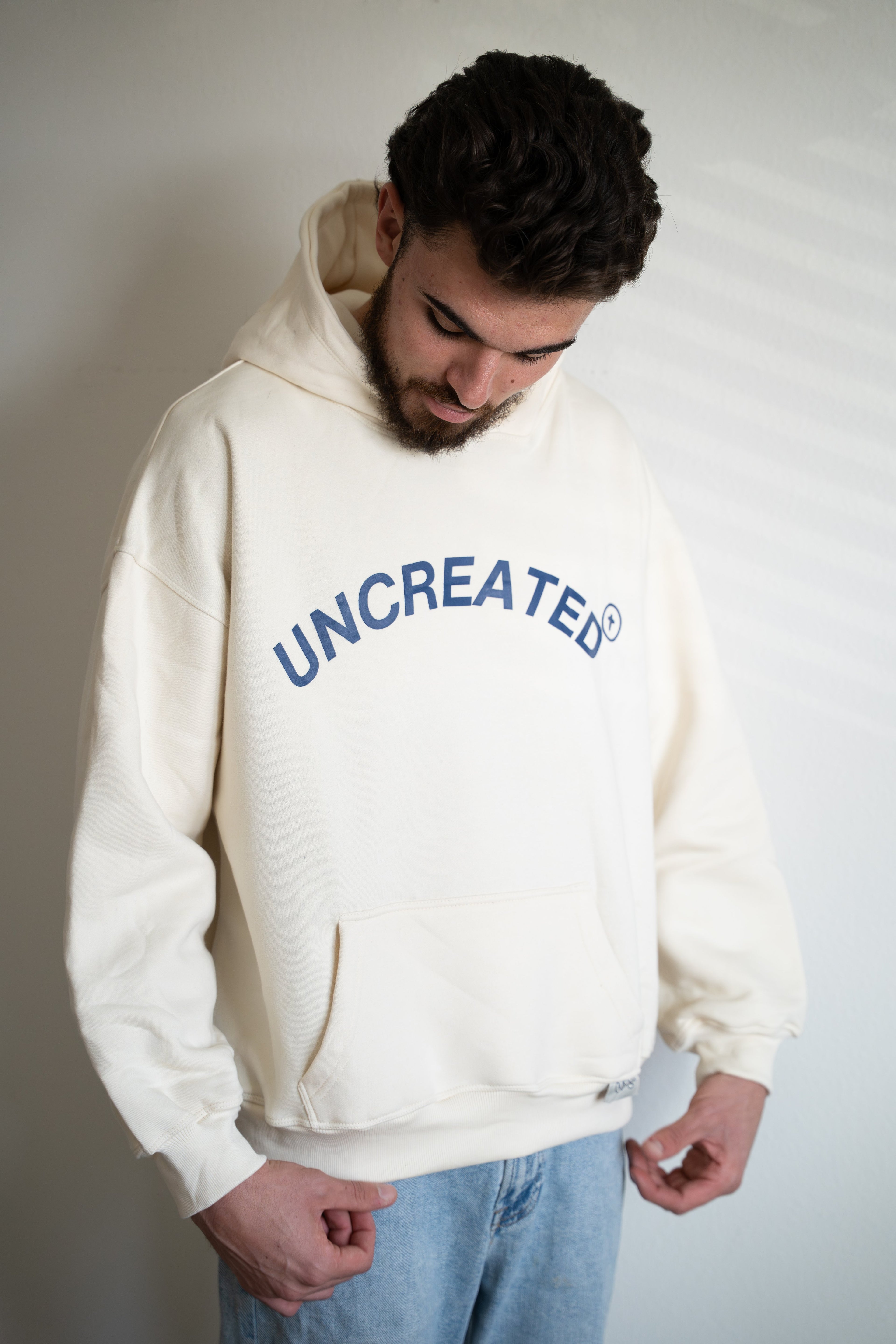 Man wearing a white hoodie with 'UNCREATED' text on a plain background. 
